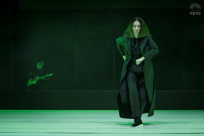 공연 실황사진(배우 이유진) 검은색 의상을 입고 머리는 긴 단발입니다. 초록색 조명이 가득한 무대 위에서 뛰어가는 포즈를 취하고 있습니다.